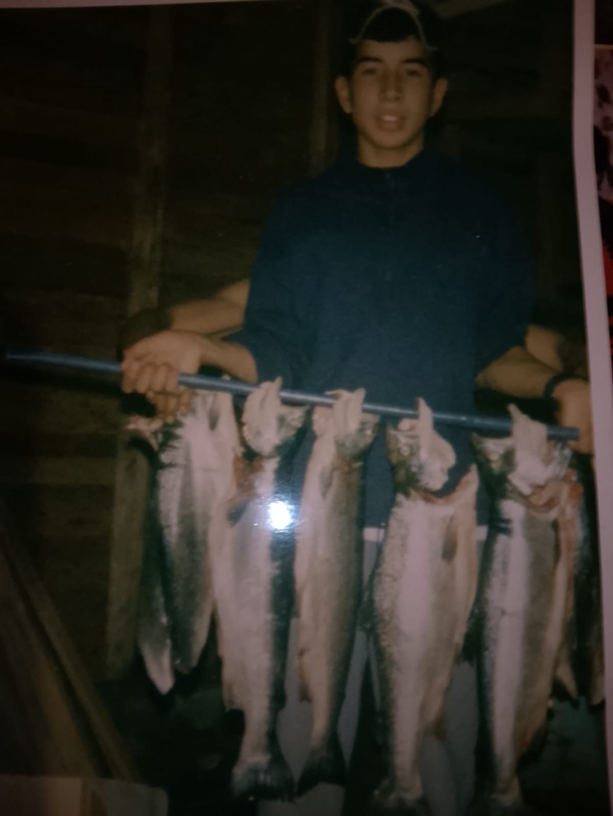A teenager in a cap holding up a pole lined with freshly caught rainbow trout