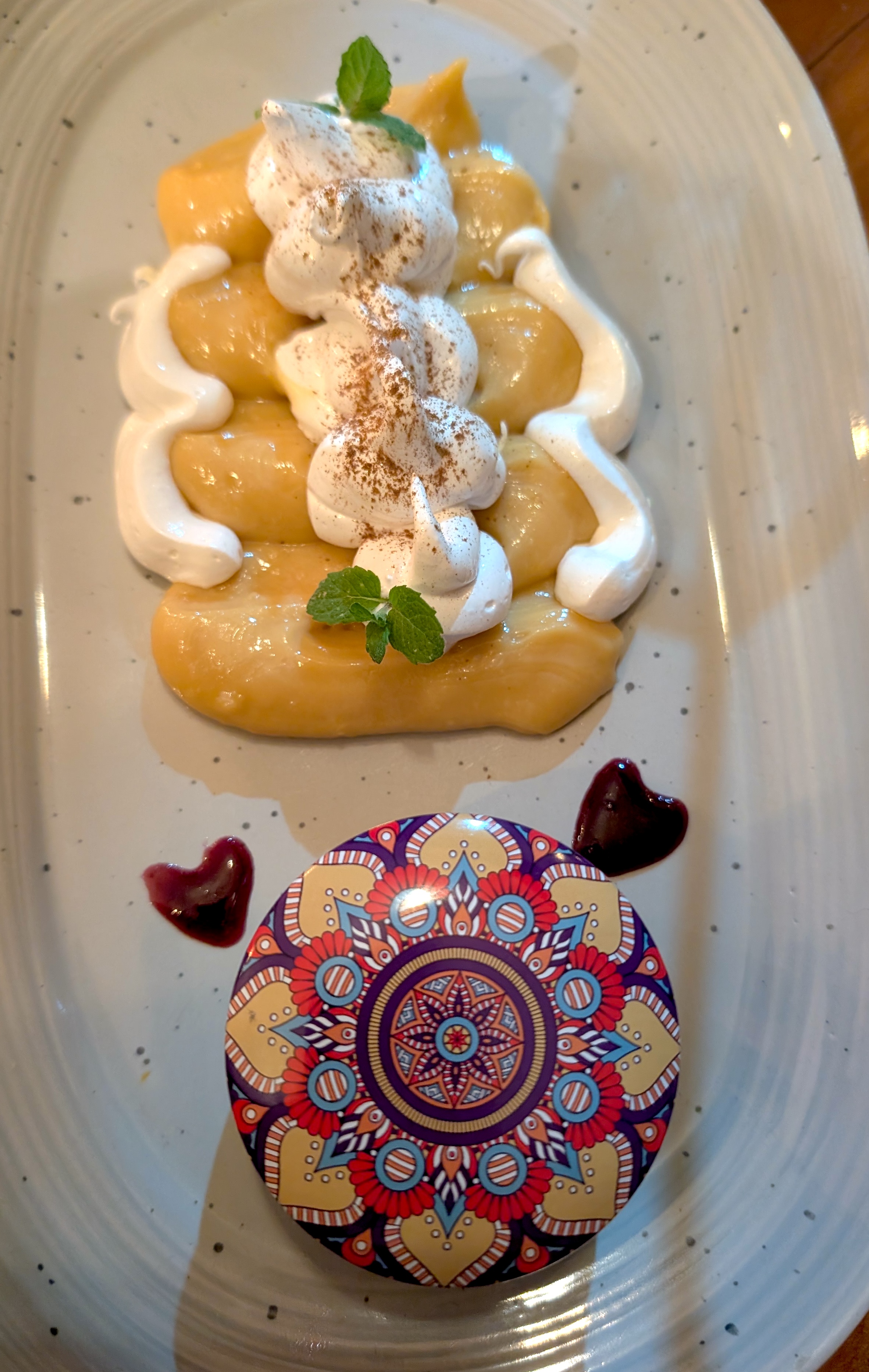 A dessert plate with meringue, mint and two berry-sauce hearts beside a mandala-patterned lid