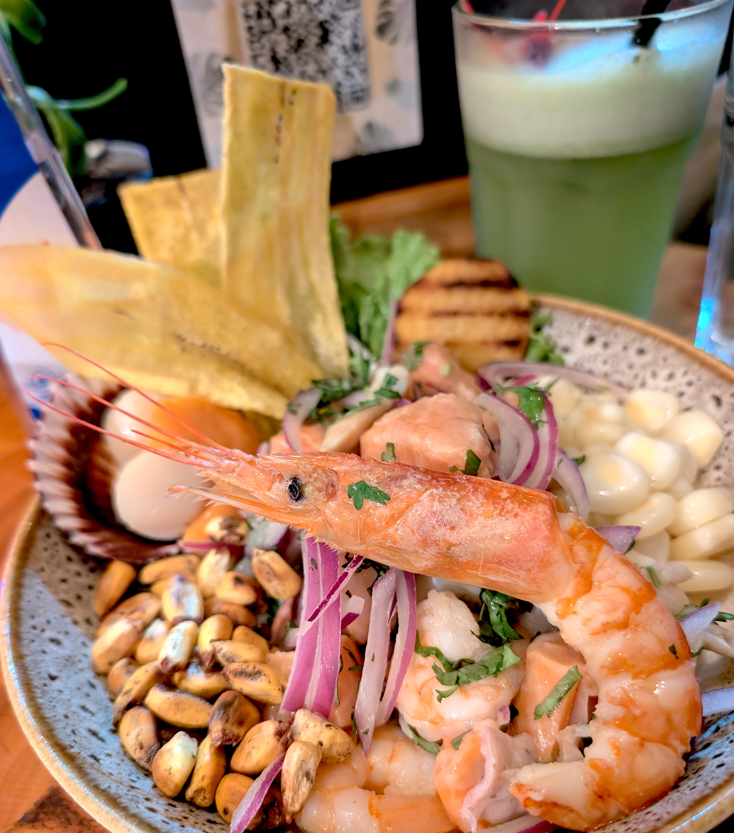 A Peruvian ceviche with a whole prawn, toasted corn and plantain chips beside a green drink