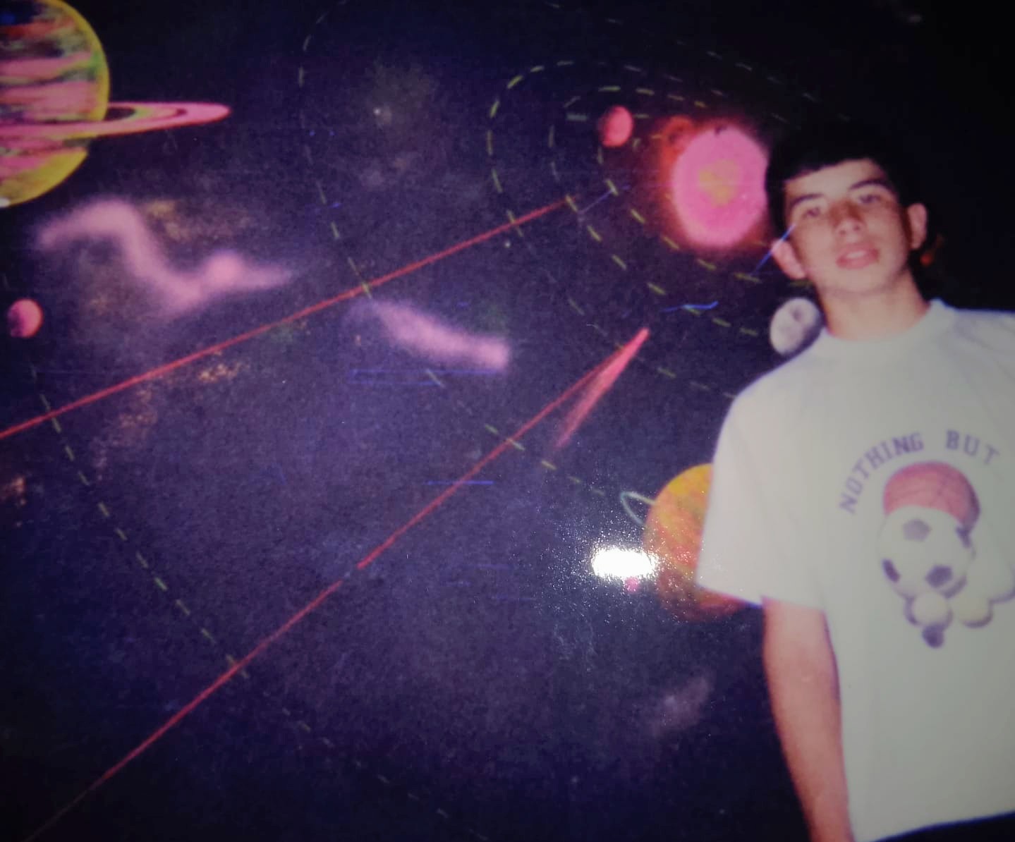 Teenage Jose Manuel in a white t-shirt in front of a painted outer-space mural