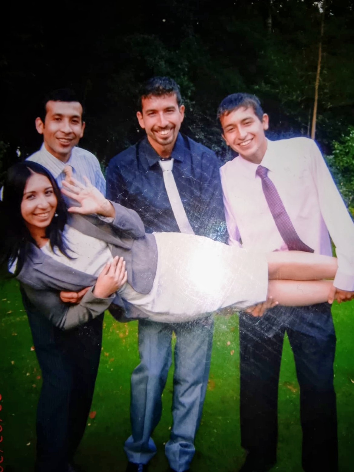 Jose Manuel and his brothers in shirts and ties, laughing as they carry their sister across a lawn
