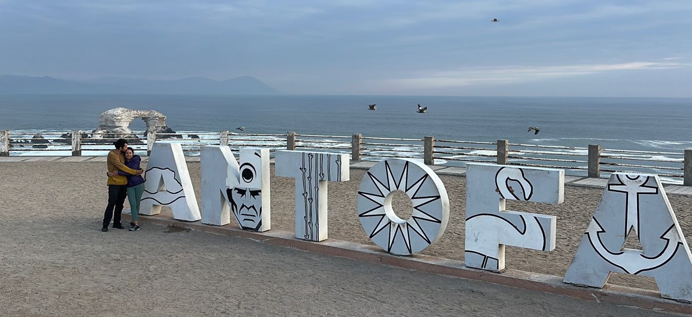 Jose Manuel and Sabah embracing beside the giant Antofagasta letters above the sea