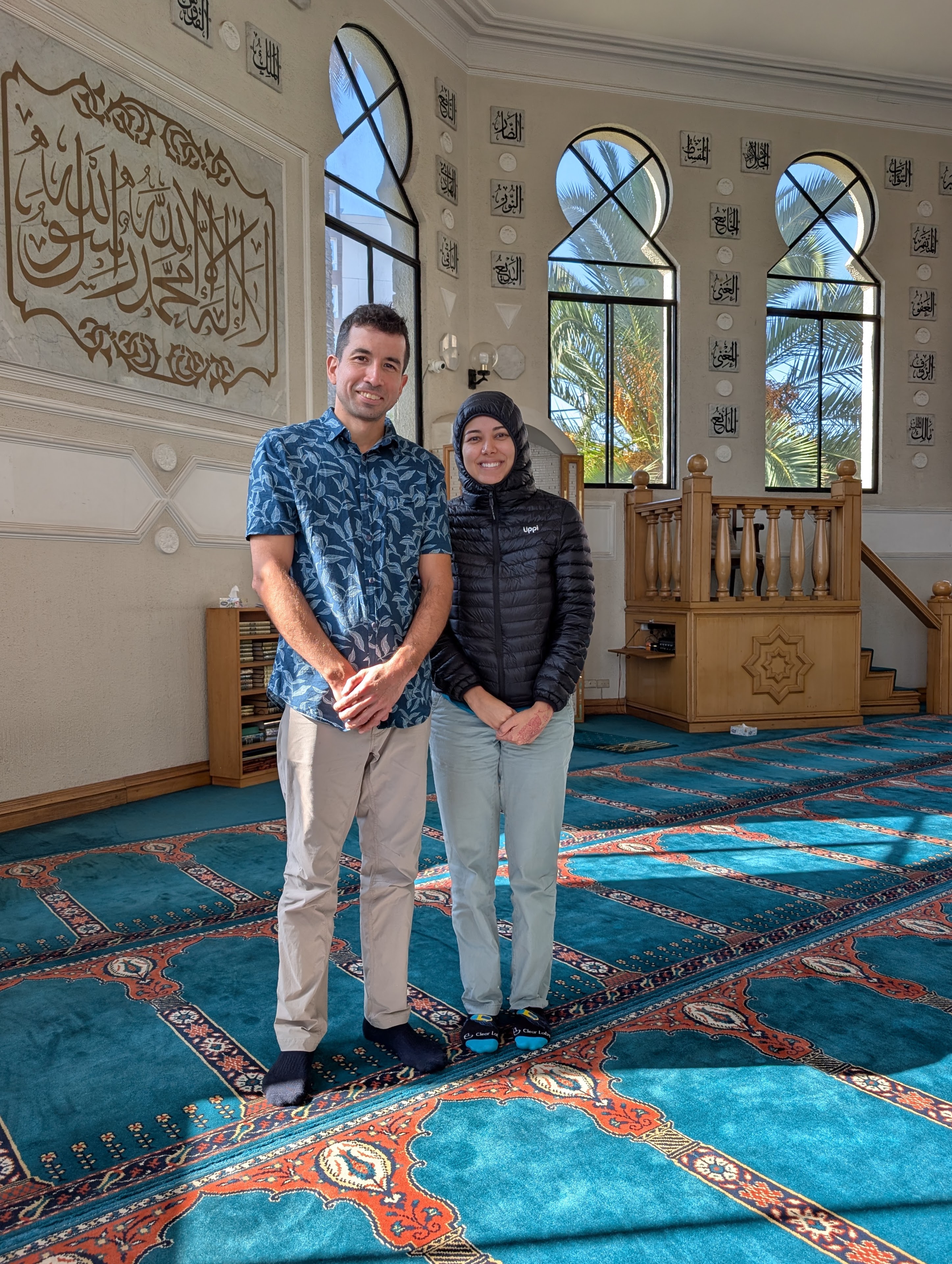 Jose Manuel and Sabah standing together inside a mosque with arched windows and a teal carpet