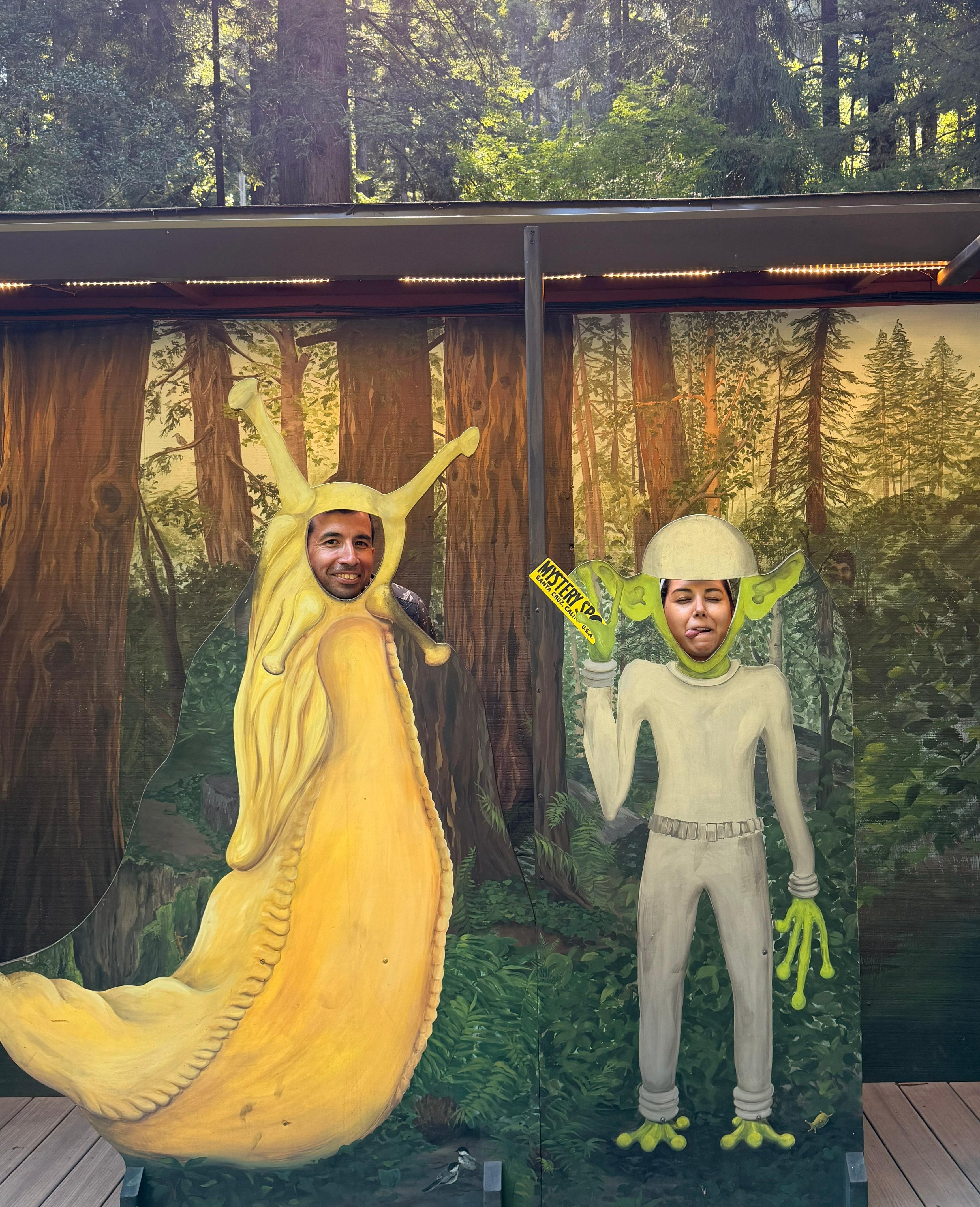 Jose Manuel and Sabah posing through banana slug and alien cutouts in a redwood forest