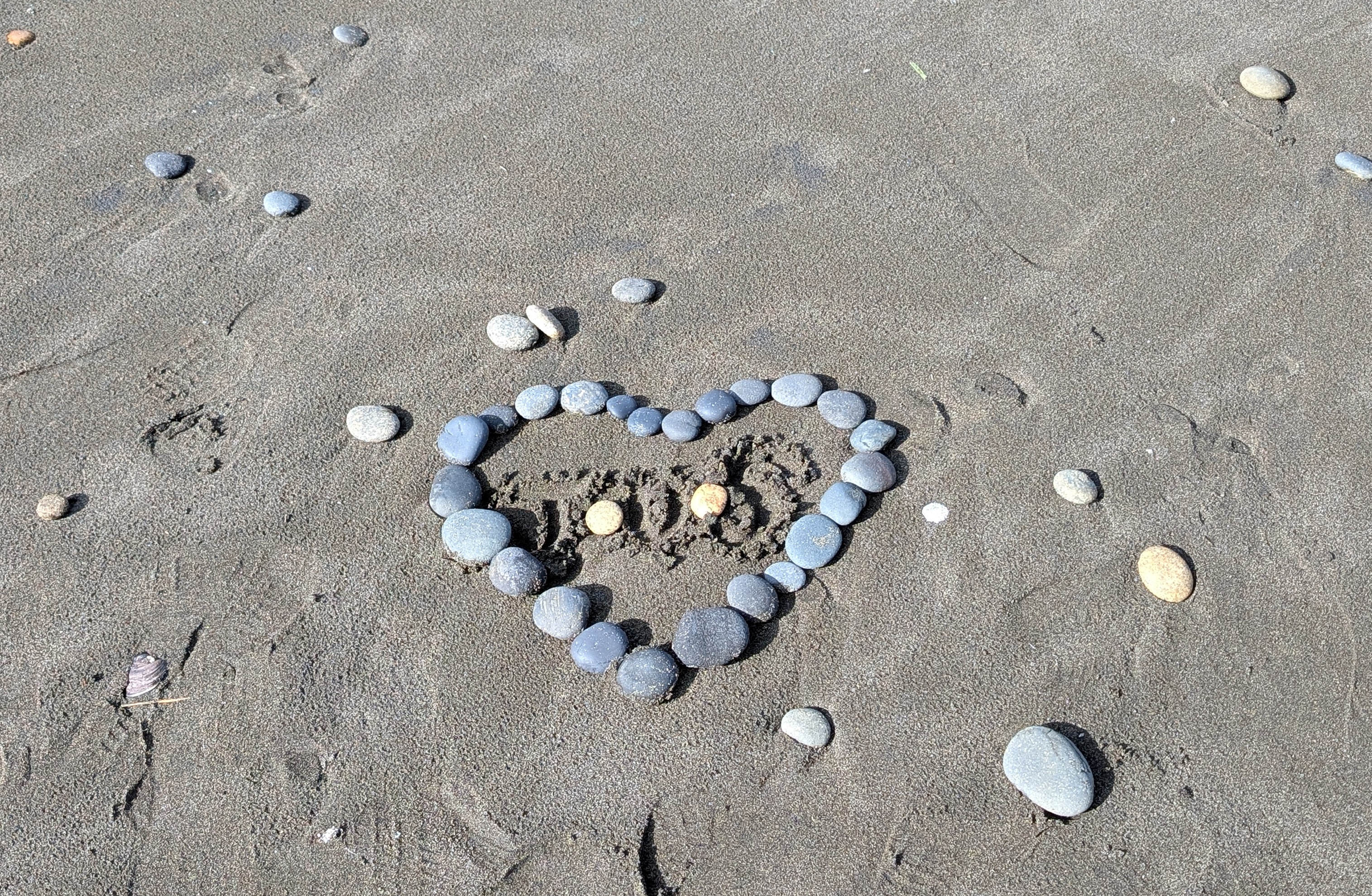 A heart made of pebbles on a dark sand beach