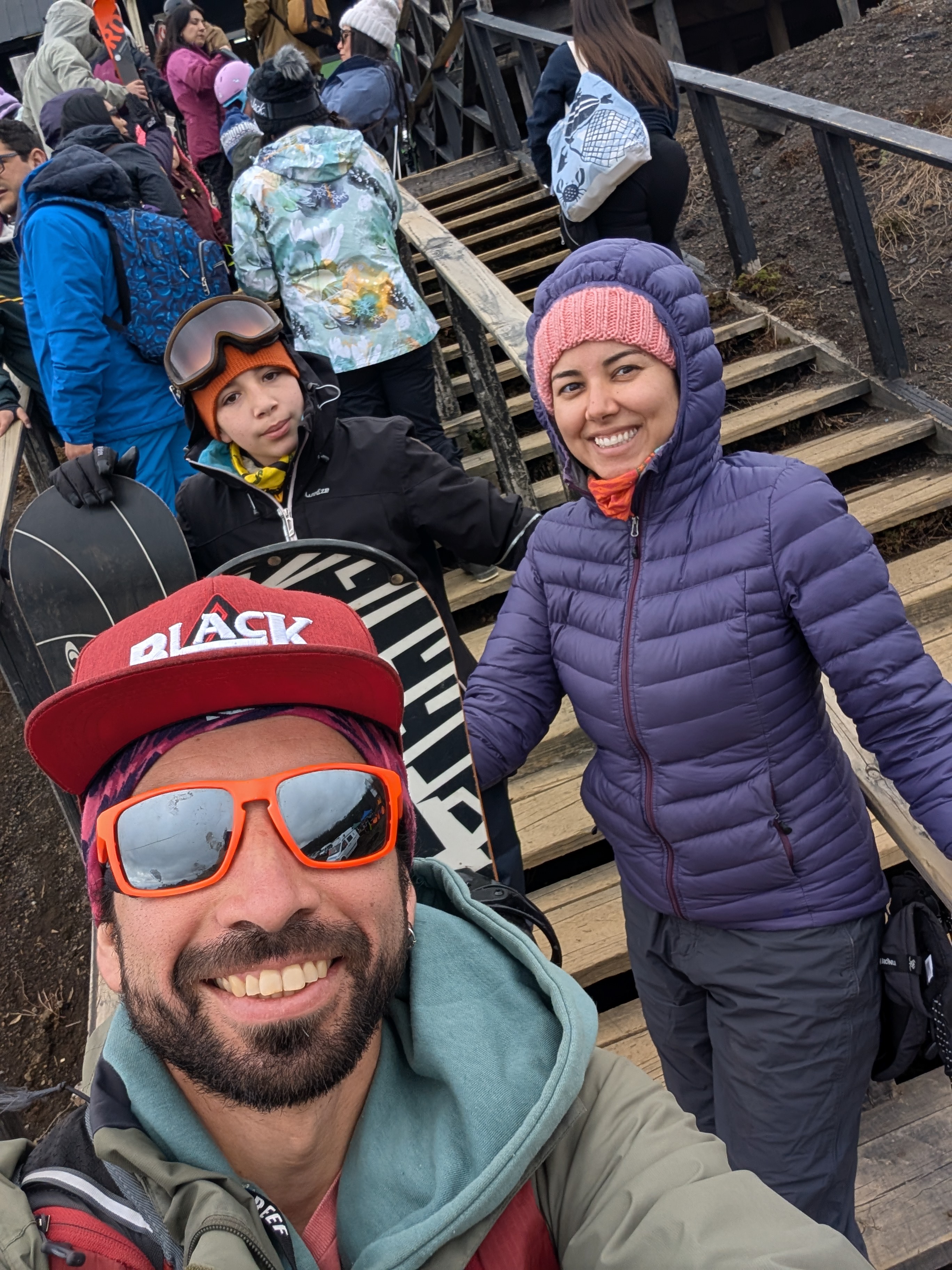 A selfie of Jose Manuel, Sabah and a young snowboarder on wooden stairs at a ski area