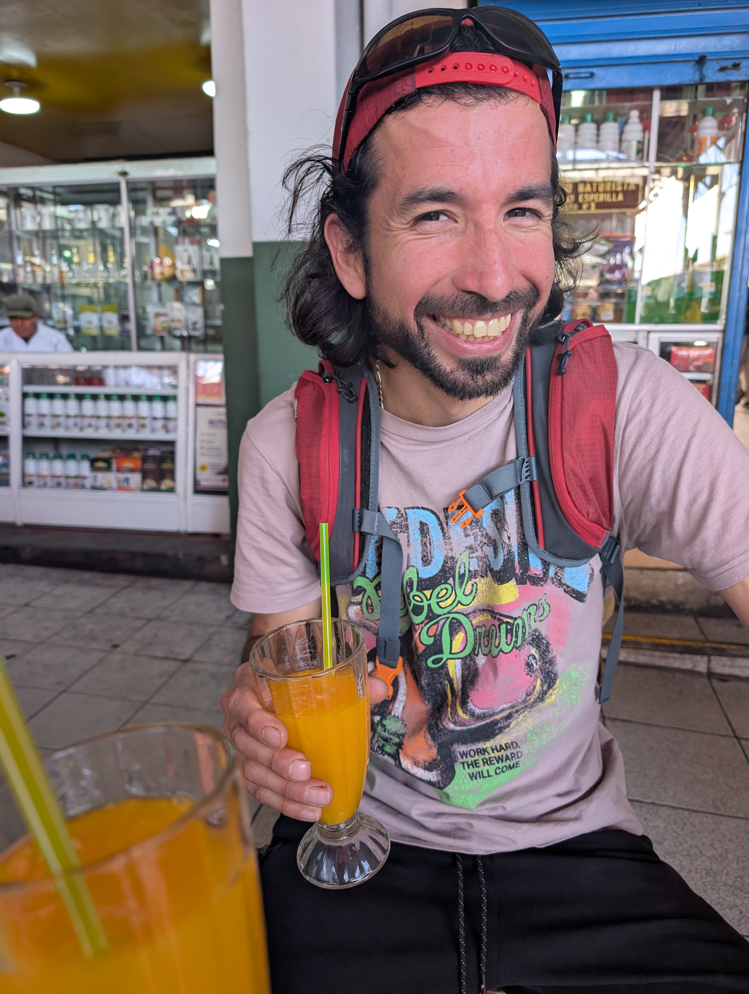 Jose Manuel grinning with a glass of fresh mango juice at a market