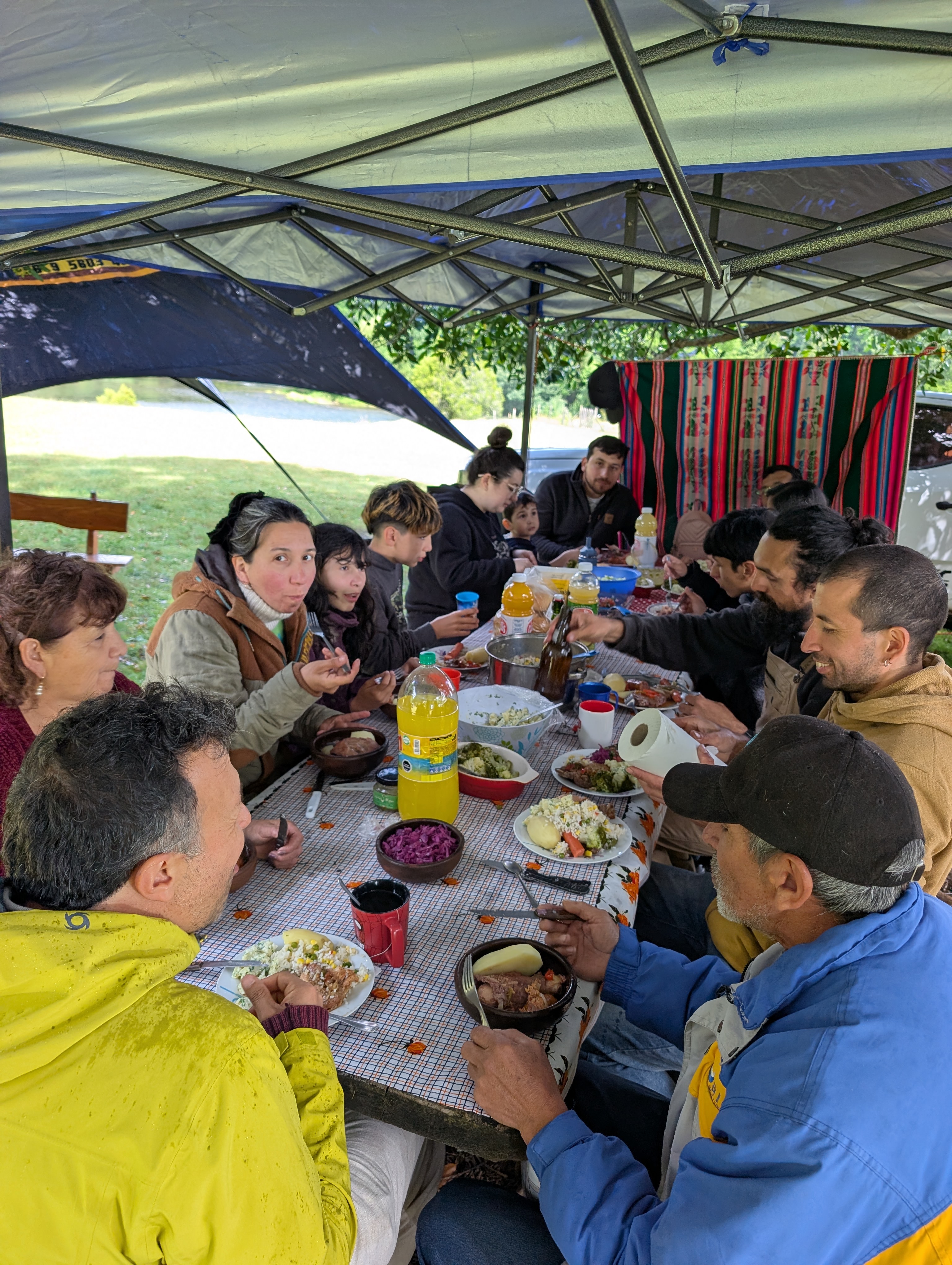 A big family lunch under a canopy tent, everyone gathered around a long table of food