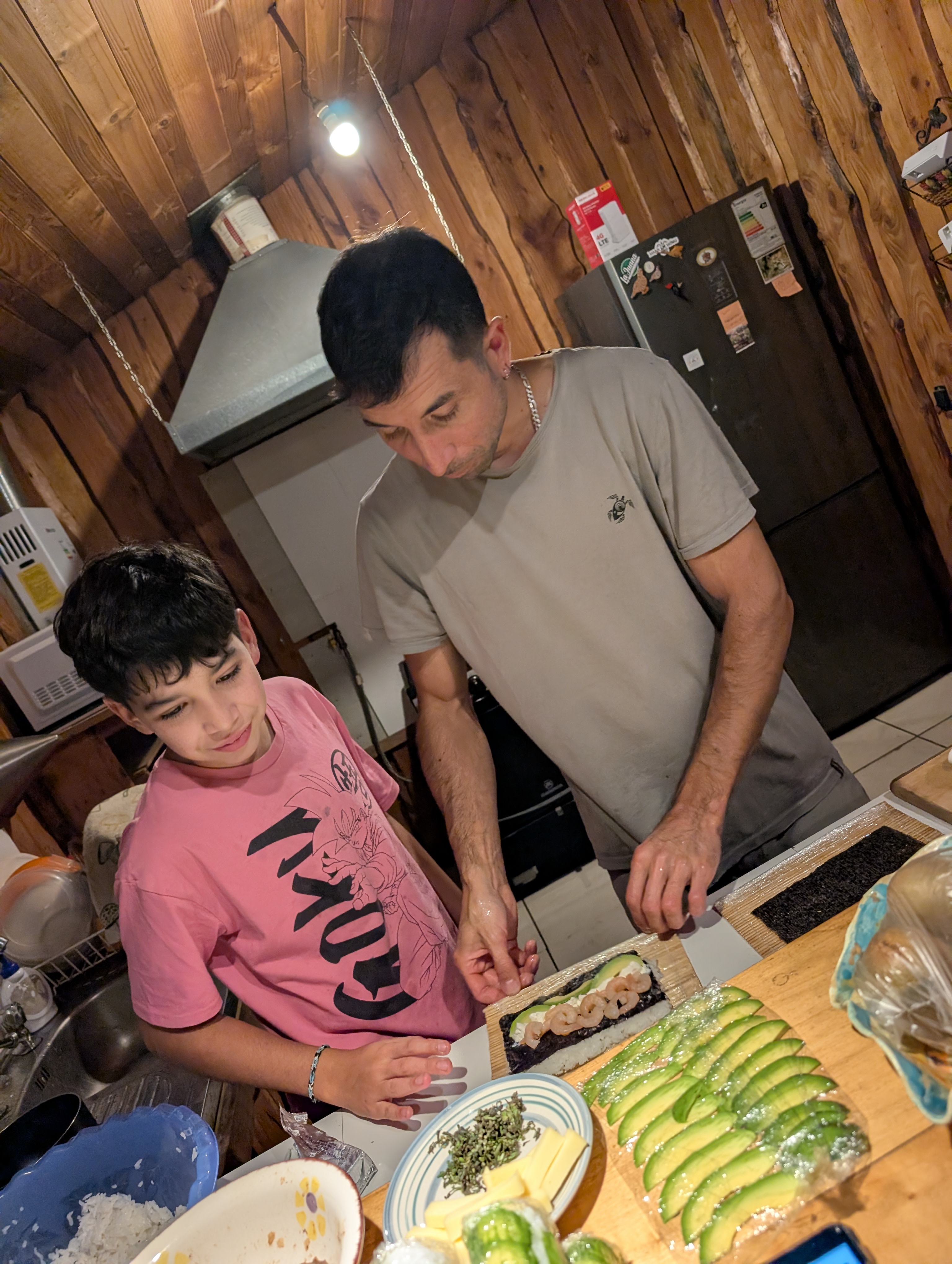 Jose Manuel rolling shrimp and avocado sushi with a young boy in a wooden cabin kitchen