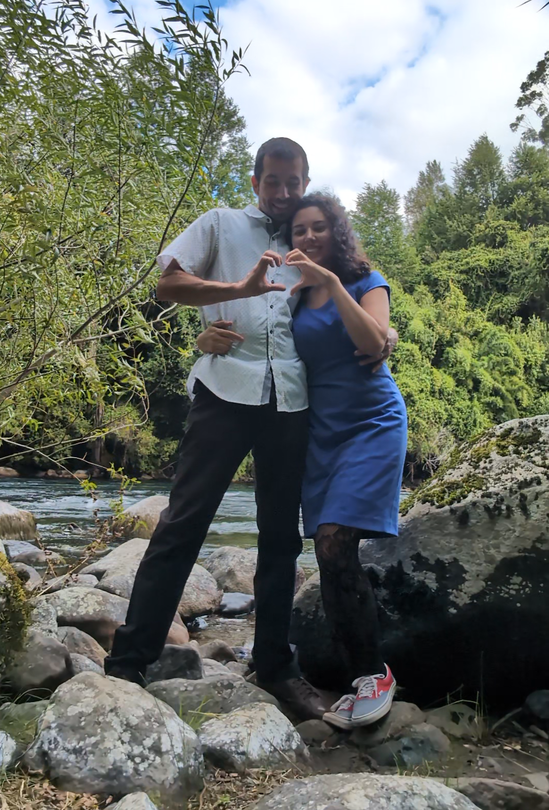 Jose Manuel and Sabah making a heart with their hands on the rocks beside a river