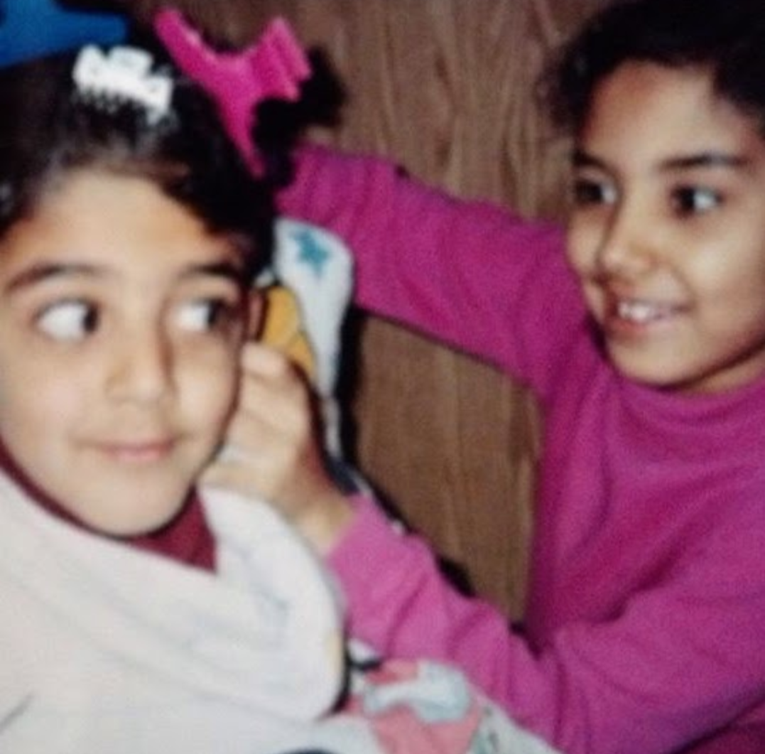 Two young sisters playing, one in a pink sweater reaching toward the other wearing hair clips