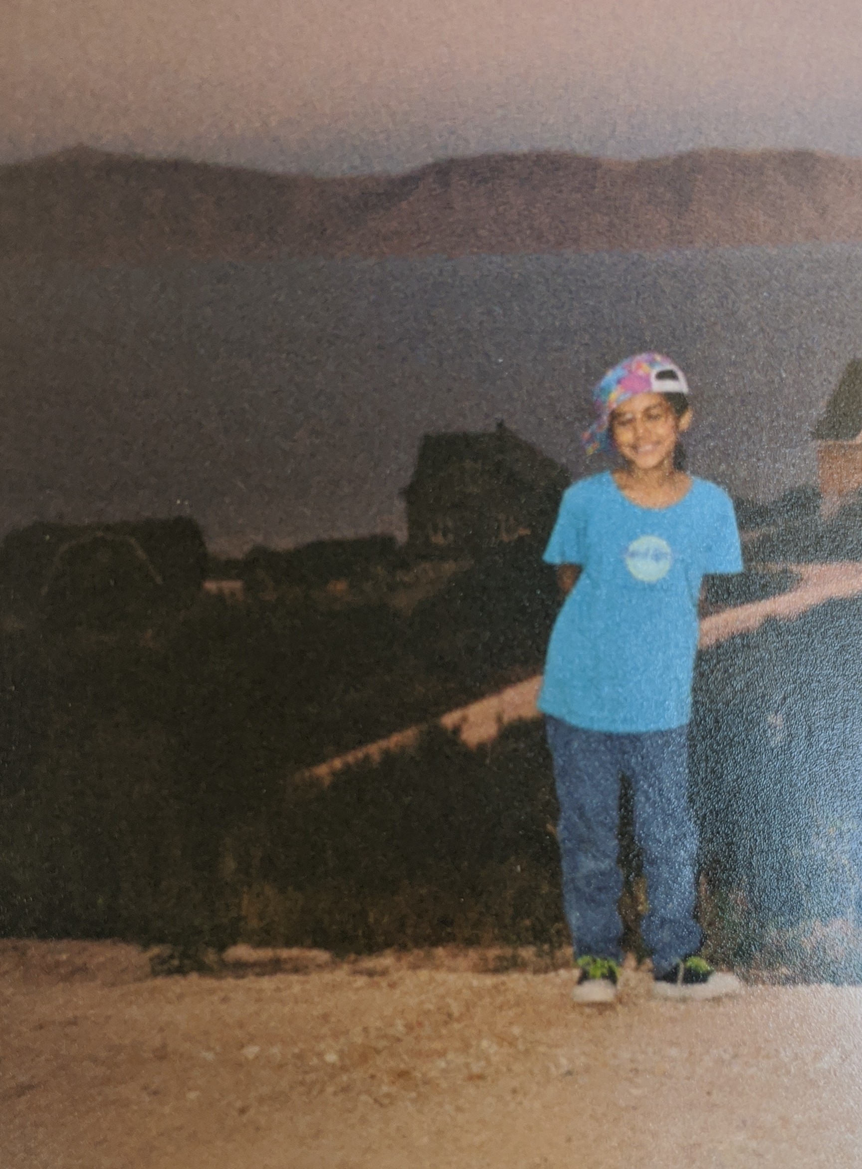 Young Sabah in a blue t-shirt and colorful cap standing on a hillside above the water