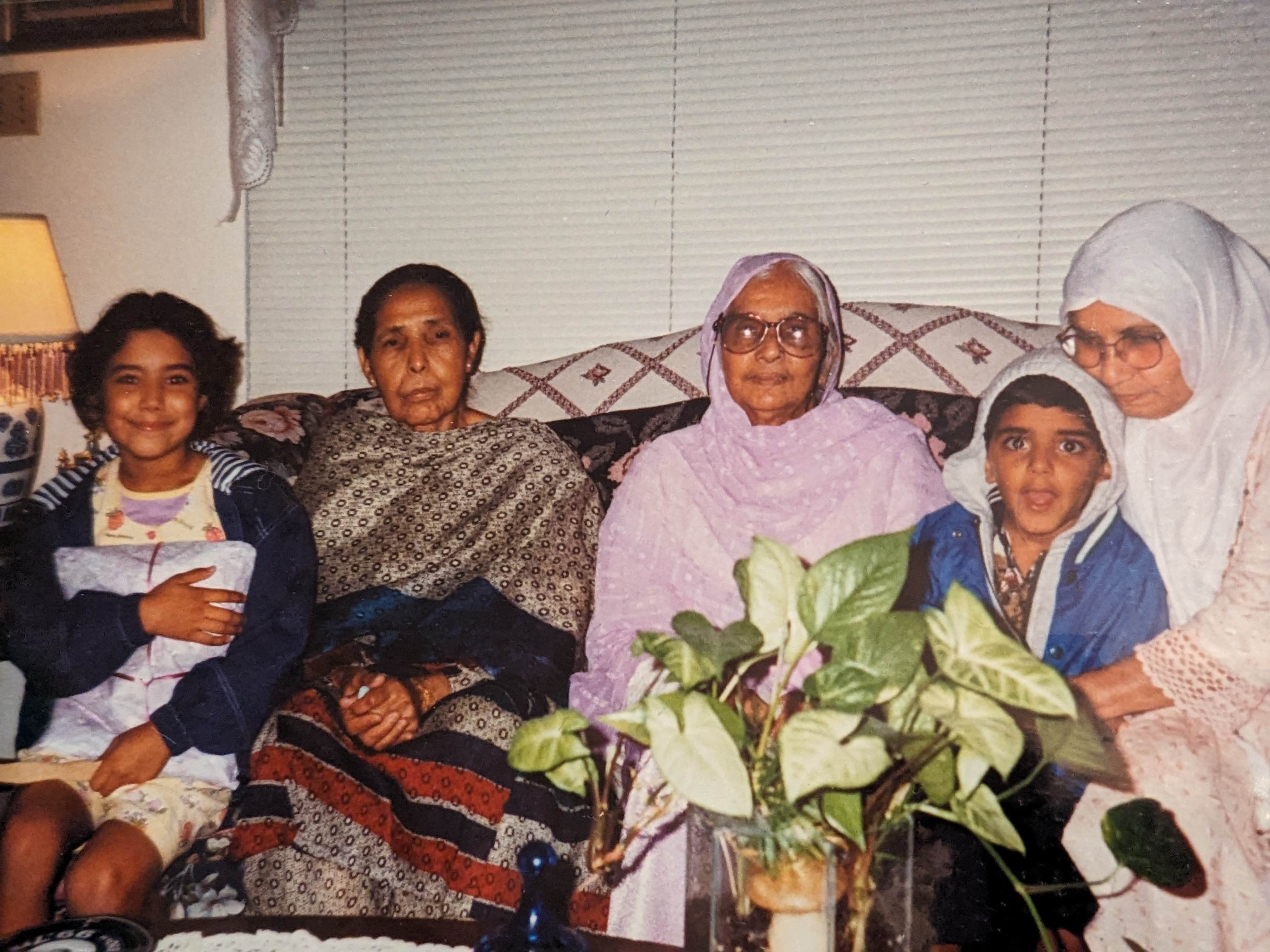 Young Sabah smiling on a sofa beside her grandmothers and a young boy