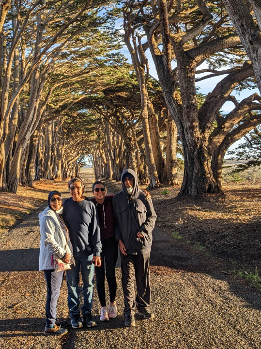 Sabah and her family standing together beneath a tunnel of cypress trees